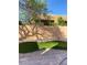 This backyard features a patch of green grass, rock landscaping, and a stone-paved patio at 10349 Mystic Pine Rd, Las Vegas, NV 89135
