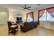 Comfortable living room with dark leather sofas, a ceiling fan, and large windows dressed with sheer and solid curtains at 768 Flowing Meadow Dr, Henderson, NV 89014
