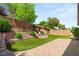 Multi-tiered backyard with terraced retaining wall, green grass, brick patio, and lush landscaping at 11764 Golden Moments Ave, Las Vegas, NV 89138