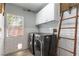 Well-lit laundry room featuring modern washer and dryer, white subway tile, wood floors, and a rustic ladder at 2434 Amoretti St, Henderson, NV 89052