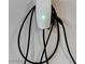 Close up of a white Tesla electric car charger with a green light on a white wall at 6618 Tangled Vines Ave, Las Vegas, NV 89139
