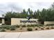 View of the Inspirada community sign with desert landscaping, flags and beautiful trees in the background on an overcast day at 2871 Tanager Hill St, Henderson, NV 89044