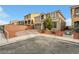 View of the home's tan exterior with desert landscaping and a brick driveway on a corner lot at 8176 Duncan Peak Ct, Las Vegas, NV 89139
