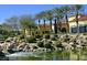 Beautiful home exterior featuring manicured landscaping, a serene pond, and mature palm trees under a clear blue sky at 4565 Riva De Romanza St, Las Vegas, NV 89135