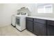 Bright laundry room featuring a modern washer and dryer, gray cabinetry and tile flooring at 9732 Abel Cliff St, Las Vegas, NV 89143
