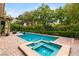 Sparkling pool with a built-in spa surrounded by a brick patio and lush landscaping, creating a serene backyard retreat at 517 Spruce Canyon St, Las Vegas, NV 89144