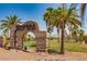 Stone archway at Chimera Golf Club entrance with palm trees and green golf course at 1113 Via Della Costrella, Henderson, NV 89011