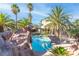 Backyard pool area featuring a rock waterfall and lush palm trees, creating a tropical oasis at 356 Clark Dr, Henderson, NV 89074