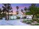 Elegant white home with arched entryway, lush landscaping, palm trees, and a circular driveway at sunset at 7185 Ranchito Cir, Las Vegas, NV 89120