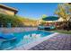 Outdoor pool area featuring lush greenery, a lounge area and an umbrella for shade at 9858 Gemstone Sunset Ave, Las Vegas, NV 89148