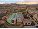 Aerial view of a luxurious community pool area with palm trees, cabanas, and mountain views at sunset at 20 Via Visione # 104, Henderson, NV 89011
