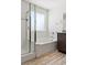 Bathroom showcasing a glass shower, soaking tub with white tile surround, and wood-style tile flooring at 438 Shimmering Sands Ave, North Las Vegas, NV 89031