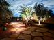 Beautifully landscaped backyard featuring stone pavers, accent lighting, mature trees, and a cozy seating area at 8316 Imperial Lakes St, Las Vegas, NV 89131