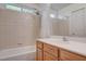 Tiled bathroom with shower-tub combo, vanity with wooden cabinets, and a bright window at 10220 Adobe Mountain St, Las Vegas, NV 89178