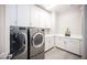 Clean laundry room with front load washer and dryer, gray tiled floors, white shaker cabinets and sink at 12018 Vento Forte Ave, Las Vegas, NV 89138