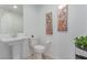 Well-lit half-bathroom with a pedestal sink, toilet, and decorative wall art, enhanced by a small potted plant at 6150 Foxes Dale St, Las Vegas, NV 89166
