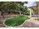 Lush backyard with artificial grass, mature trees, stone patio, and a covered area with comfortable seating at 801 Aquitaine Ct, Las Vegas, NV 89145