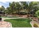 Landscaped backyard featuring tiered planting beds, mature trees, artificial grass and a stone patio area with seating at 801 Aquitaine Ct, Las Vegas, NV 89145