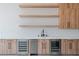 Modern wet bar with beverage coolers, sink, wood cabinets, and white backsplash at 8721 Robinson Ridge Dr, Las Vegas, NV 89117