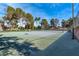 Wide view of a pristine tennis court complemented by mature trees and well-kept landscaping at 3455 Five Pennies Ln, Las Vegas, NV 89120