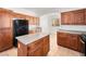 Kitchen features wood cabinets, speckled countertops, tile floors, kitchen island, and black fridge at 16 Goldleaf Falls Ave, North Las Vegas, NV 89031