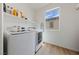 Well-lit laundry room with modern white washer and dryer, window, and overhead shelving at 2606 Marvel Astoria St, Henderson, NV 89044