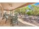 This covered patio features an outdoor dining table set, ceiling fans, and views of the rock-covered yard with lush trees and shrubbery at 10314 Premia Pl, Las Vegas, NV 89135