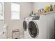 Well-lit laundry room with a side-by-side washer and dryer and shelving above for storage and a sleek trash receptacle at 10196 Sequoia Glen Ave, Las Vegas, NV 89166