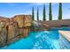 Beautiful pool with rock waterfall feature, surrounded by lush greenery and a clear blue sky at 12219 Crystal Shore Ave, Las Vegas, NV 89138