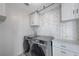 Well-lit laundry room with gray washer and dryer, white cabinets, and stylish brick accent wall at 6276 Point Isabel Way, Las Vegas, NV 89122