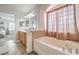 Bright bathroom featuring a large bathtub, window with curtain, and vanity with wooden drawers at 10294 Running Falls St, Las Vegas, NV 89178