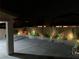 A nighttime view of a backyard with a concrete patio, accented by a white picket fence and ambient lighting at 6442 Kobe Knoll Ct, Las Vegas, NV 89141