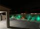 A nighttime backyard view features a concrete patio and white picket fence, enhanced by vibrant outdoor lighting at 6442 Kobe Knoll Ct, Las Vegas, NV 89141