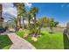 Landscaped backyard featuring synthetic grass, tall palm trees, seating, and a paved walkway on a sunny day at 10408 Mezzanino Ct, Las Vegas, NV 89135