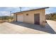 A detached garage with a white door and beige stucco exterior sits beside a concrete driveway under a blue sky at 4691 Sun Valley Cir, Las Vegas, NV 89122