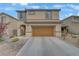 Two-story home featuring a tan exterior, two-car garage, and low maintenance desert landscaping at 2445 Rue Royale, Henderson, NV 89044