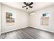 Well-lit bedroom with gray wood floors, neutral walls, a ceiling fan, and two large windows at 266 Tungsten St, Henderson, NV 89015