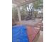 A backyard with a blue tarp, a brick patio with furniture, trees, and a decorative rock border at 7894 W Patrick Ln, Las Vegas, NV 89113