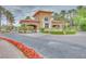 Community entrance with stone gatehouse, mature landscaping, and vibrant red flowers at 65 Bellissima Lago Ct, Henderson, NV 89011