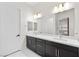 Bathroom with double vanity sinks, dark cabinets, and a large mirror on white tile flooring at 717 Monroe Hill Pl, Henderson, NV 89011