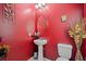 Stylish powder room featuring a pedestal sink, oval mirror, and bold red walls at 9457 Alma Ridge Ave, Las Vegas, NV 89178
