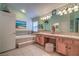 Bright bathroom featuring a soaking tub, double sinks, neutral tile, and a large countertop with vanity at 1532 Via Cassia, Henderson, NV 89052