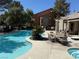 Community pool area featuring a clear blue pool, lounge chairs, dining area, and lush tropical landscaping at 555 E Silverado Ranch Blvd # 2052, Las Vegas, NV 89183