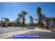 View of the community gate featuring desert landscaping, palm trees, and stucco homes on a sunny day at 9710 Geiger Peak Ct, Las Vegas, NV 89148