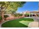 Large backyard with artificial lawn, covered patio, mature trees, and a brick wall at 1506 Camino Summit Ave, Henderson, NV 89012