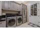 Well-lit laundry room featuring gray cabinetry, a black countertop, stainless steel appliances, and a tiled floor at 52 Innisbrook Ave, Las Vegas, NV 89113
