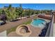 Aerial view of a kidney-shaped pool and raised hot tub, surrounded by a brick patio and artificial turf at 7380 Abundant Harvest Ave, Las Vegas, NV 89131