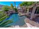 Luxurious backyard pool with rock waterfall features, tropical plants, and a covered patio with comfortable seating at 11359 Winter Cottage Pl, Las Vegas, NV 89135