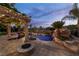 Inviting pool area at twilight, boasting a rock waterfall, lush landscaping, and a cozy fire pit at 11359 Winter Cottage Pl, Las Vegas, NV 89135