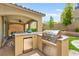 Outdoor kitchen with stainless steel BBQ, mini fridge, stone countertops, and covered seating area at 419 Vigo Port St, Las Vegas, NV 89138